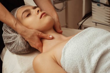 Kozmetik şapkayla kanepede uzanmış, kaplıca salonunda gözleri kapalı güzel bir kız. Masör sağlıklı yaşam prosedürleri uyguluyor, vücudu canlandırıyor. Yüksek kalite fotoğraf