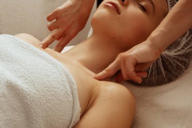 Kozmetik şapkayla kanepede uzanmış, kaplıca salonunda gözleri kapalı güzel bir kız. Bir masör masaj prosedürleri, rahatlama, vücut canlandırma yapar. Yüksek kalite fotoğraf