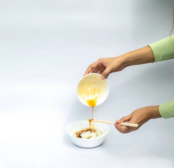 Stock image Hands of asia women hold up fresh egg is mixing with soy sauce and hold chopstick while pouring into the Japan rice bowl on white background