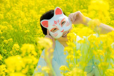 Kedi maskesi takan Japon kadın, güzel sarı çiçeklerde ya da Japonya 'da açan Nanohana' da bahar mevsiminin tadını çıkarıyor..