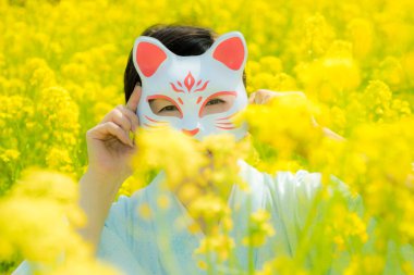 Kedi maskesi takan Japon kadın, güzel sarı çiçeklerde ya da Japonya 'da açan Nanohana' da bahar mevsiminin tadını çıkarıyor..