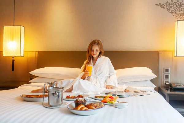 Food in bed serve in luxury hotel. Woman on vacation enjoy breakfast in bed in hotel room, drinking orange juice, eating food and relaxing on holidays. Room Service