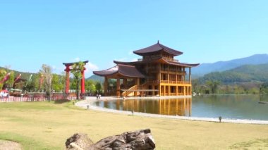 Geleneksel Japon ahşap evinin yeşil bahçesi, sakin göleti, kırmızı torii kapısı ve yaz gününde yeşil tepeleri olan sinematik videosu. Japonya tarzı tapınak veya tematik parkta sergi