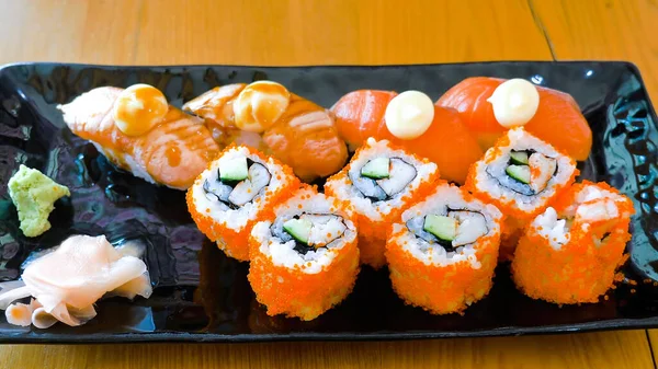 Sushi set in japanese restaurant. Asian food. Various kinds of delicious sushi rolls with salmon, grilled fish and crab sticks on black plate in cafe. Assorted sushi nigiri and maki