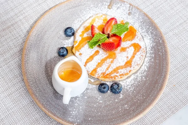 Delicious buttermilk pancake with fresh berries and maple syrup in small jug. Tasty sweet food on breakfast in hotel or cafe. Dessert with strawberry and blueberry.