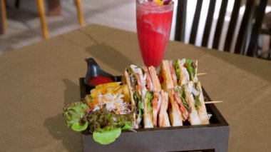 Tahtada dört sandviç var. Jambonlu sandviç, domates, marul, kızarmış ekmek patates kızartması ve ketçap sosuyla servis ediliyor. Kafedeki ahşap masada kulüp sandviçi..