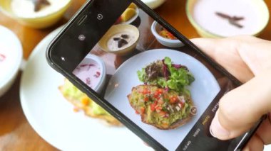 Erkek eller sağlıklı vejetaryen kahvaltısı ya da akşam yemeğini akıllı telefondan çekiyor. Erkek kişi cep telefonu tutuyor ve sosyal ağ için yemeğini çekiyor. Lokantadaki blog yazarı içerik oluşturur
