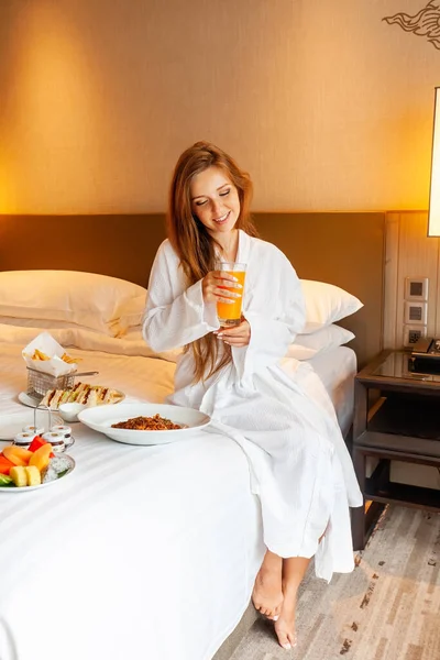 Food in bed serve in luxury hotel. Woman on vacation enjoy breakfast in bed in hotel room, drinking orange juice, eating food and relaxing on holidays. Room Service