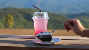 Dışardaki kafede kaşık kaşık çikolatalı kek yiyen bir kadın. Sıcak yaz gününde doğaya güven. Buzlu soğuk içecek ve bir dilim tatlı pasta..