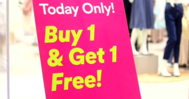 衣料品店での販売促進 黄色の単語と明るいピンクの看板購入1取得1現代のショッピングモールで無料 看板は季節の黒金曜日割引で立つ — ストック動画