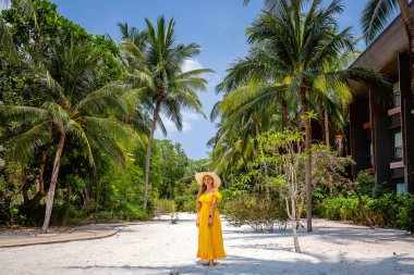 Seyahat eden kadın, tropik tatil beldesinde. Parlak sarı elbiseli ve hasır şapkalı mutlu genç bayan gezgin lüks Palm Beach tatil beldesinde yaz tatilinin tadını çıkar. Tayland 'a gezi