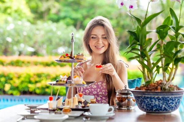 若い女性は甘いタルトケーキを食べ 屋外のプールサイドカフェやレストランに設定されたアフタヌーンティーとテーブルに座っています 夏休み休暇のコンセプト — ストック写真