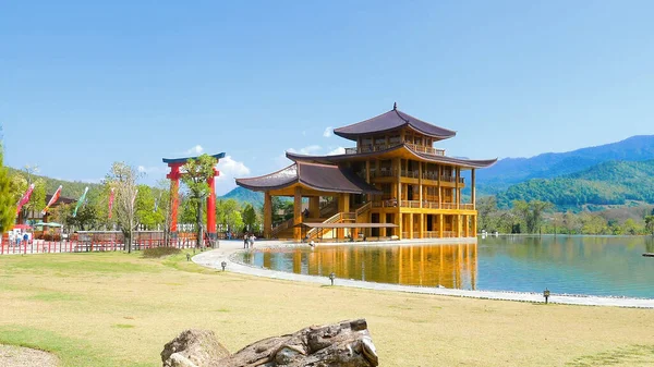 stock image Cinematic video of traditional Japanese wooden house with green garden, calm pond, red torii gate and green hills on background in summer day. Japan style temple or exhibition in thematic park