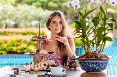 Genç bir kadın tatlı tart keki yer, açık havuz kenarındaki kafede ya da lüks tropikal otellerde ya da havuz geçmişi olan otellerde çay eşliğinde masaya oturur. Yaz tatili, tatil konsepti.