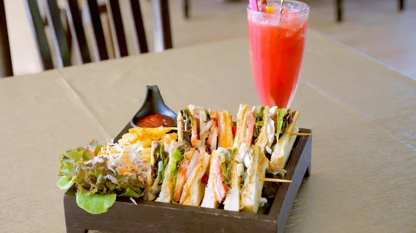 Club sandwich with ham, tomato and toasted bread with french fries, green fresh salad and watermelon shake in cafe. Four sandwiches on a rustic wooden table in traditional American cafe or restaurant.