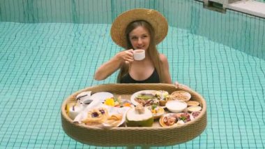 Genç bir kadın tropik bir villada tatilde dinleniyor. Gezgin yüzme havuzunda yüzen kahvaltıdan kahve içiyor. Lüks otelde kahvaltı, otelde sabah. Asya seyahati, yaz tatili.