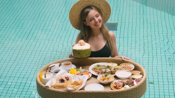 在游泳池里戴着草帽 带着早餐盘的旅行妇女 拿着年轻的椰子 在炎炎夏日享受着完美的天气 泰国的度假别墅 — 图库视频影像