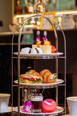 Traditional afternoon tea stand with fancy table set with sandwiches, macaroons, cakes and other sweets. Hotel or restaurant, showcasing luxurious and elegant atmosphere. Food, dining, and hospitality