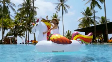 Woman ride and fun on inflatable toy in swimming pool at luxury hotel resort with palm trees. Travel girl in swimwear celebrating and enjoying summer vacation at sunny day on tropical holiday.