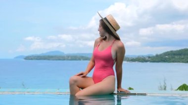 Tropikal tatilde olan bir kadın lüks bir otelin havuzunda, arka planda okyanus olan bir havuzda dinleniyor. Yaz tatilindeki kadın gezgin tatil gününün tadını çıkarıyor. Yavaş çekim