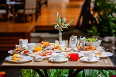 Table full of various fresh food in luxury modern restaurant in hotel. Delicious dishes, including fruits, pastries, and cooked meals on table. Restaurant setting. Breakfast or morning meal