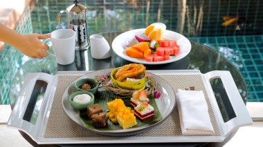 Breakfast in luxury Hotel with Table Full of Various Food - Fruits, Pastries, Eggs, Juices, and Coffee near Green Lake on Summer Sunny Day. Morning Food and Asia Travel Concept