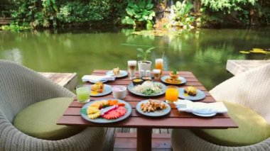 Breakfast in luxury Hotel with Table Full of Various Food - Fruits, Pastries, Eggs, Juices, and Coffee near Green Lake on Summer Sunny Day. Morning Food and Asia Travel Concept