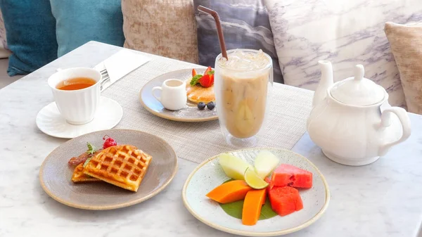 Hotel breakfast includes refreshing iced coffee, colorful fresh fruits, delicious waffles and pancakes with berries. Bright and colorful morning in resort, tropical vacation.