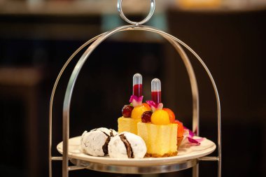 Traditional afternoon tea stand with fancy table set with sandwiches, macaroons, cakes and other sweets. Hotel or restaurant, showcasing luxurious and elegant atmosphere. Food, dining, and hospitality
