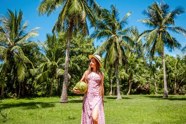 Travel happy woman in straw hat and dress relaxing on summer vacation on tropical paradise island among coconut palm trees. Happy traveller woman enjoys her Thailand exotic trip. Wanderlust concept