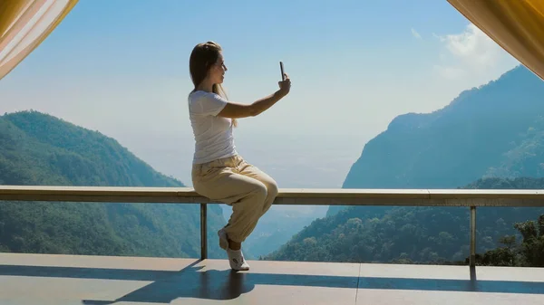 Travel blogger woman broadcasts live on mobile phone with beautiful mountain view in background. Life and work of influencers, travel, outdoor lifestyle, camping and vacation