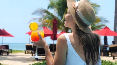 Çekici genç turist kadın yüzme havuzunda içecek kokteyli içiyor, denizin, palmiye ağaçlarının ve sahil manzarasının tadını çıkarıyor. Mutlu gülümseyen kız rahatlama tesisi ve alkolsüz içki. Phuket, Tayland