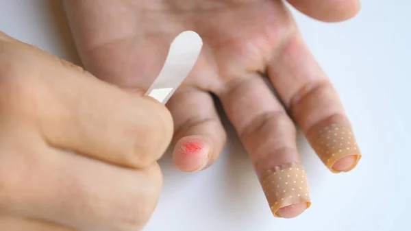 Man applying band aid patch on cuts wound on fingers. Male putting medical adhesive bandage tape sticking plaster to injured sore finger. First aid after accident, self cure help concept. Close-up.