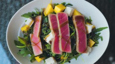 Servis tabağında mango, peynir ve roka ile taze çiğ ton balığı salatası. Keto ya da paleo diyetleri için mükemmel. Sağlıklı, protein dolu bir yemeğin üst görüntüsü..