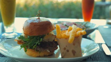 Close-up of beef burger on restaurant table with bacon and cheese. Tasty American food. Delicious grilled cheeseburger with fries served at the restaurant. Unhealthy but satisfying.