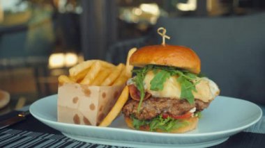 Tasty gourmet beef burger with salad, cheese and bacon on table. Deliciously grilled, served in a restaurant. Unhealthy food. American traditional food. Close up.
