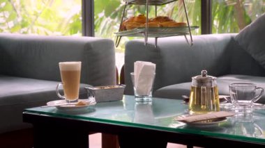 Waiter put tiered afternoon tea stand with elegance pastries and delicate sandwiches, lush tropical greenery in background in luxury hotel restaurant. Served delicious sweet food.