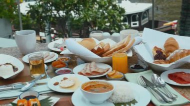 Hotel breakfast with river view. Morning food in luxury outdoor restaurant. Fresh pastry, ham, sausage, cheese, juices on table with boats on background. Various buffet food in hotel.
