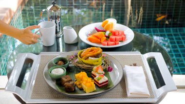 Breakfast in luxury Hotel with Table Full of Various Food - Fruits, Pastries, Eggs, Juices, and Coffee near Green Lake on Summer Sunny Day. Morning Food and Asia Travel Concept