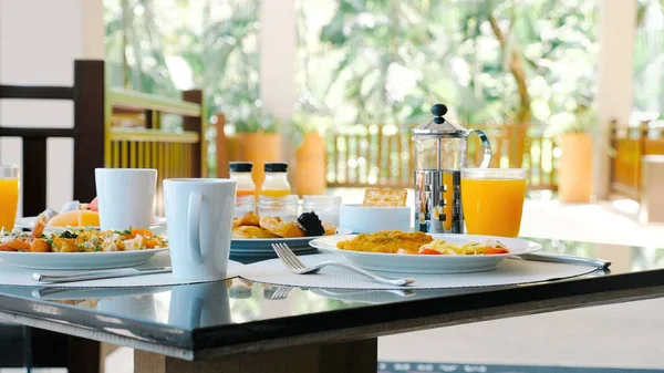 Tropical breakfast buffet at hotel. Fresh food and juices served in luxury outdoor restaurant with palm trees on background. Perfect vacation breakfast.