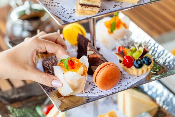英语午后茶与甜早餐小吃为乐 仪式上展示了精美的甜点和糖果 一个女人的手从茶摊上选了一份甜点 图库图片