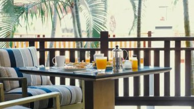 Breakfast at luxury tropical hotel with a buffet of fresh food and juices. Served outdoors amidst palm trees in the background. Luxury vacation breakfast.