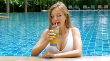 Beautiful woman in white swimsuit lounging in swimming pool, drink cocktail. Perfect for summer pool resort or spa hotel promotions. Portrait of smiling and relaxed female model enjoy tropical drink