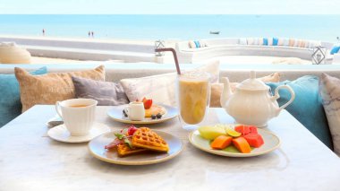 Beachfront hotel breakfast, beautiful morning on beach. Enjoy delicious meal with sea view. Relax and enjoy ocean and sound of waves. Beach, vacation, tropical holidays, travel.