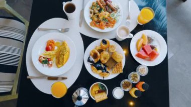Varied buffet breakfast at tropical hotel. Top view of fresh pastries, eggs, fruits, juices, and coffee on table. Colorful spread with tropical fruits and tea.