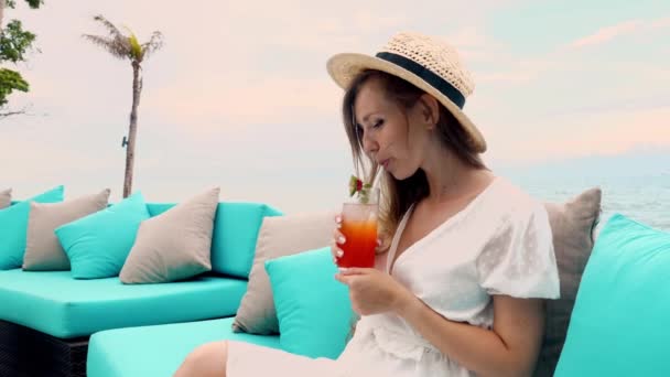 ノンアルコールカクテルを飲みながら美しい海の景色を眺めながら タイのプーケットのビーチソファでリラックスしたわら帽子の旅の女性 タイでの休暇 幸せな若いです女性上の熱帯夏休み — ストック動画