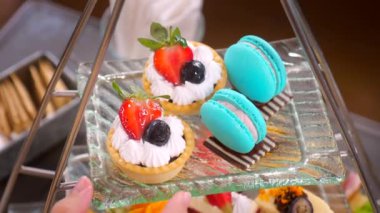 Close up of Woman hand take a dessert tartlet with fresh berries from sweet traditional Afternoon tea stand in restaurant. Colorful delicious sweet food.