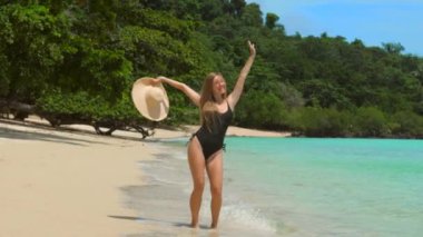 Happy woman having fun, jumping and dancing on tropical beach, celebrate vacation. Funny female tourist enjoying summer holidays, vacations, sunny day, sea view on background