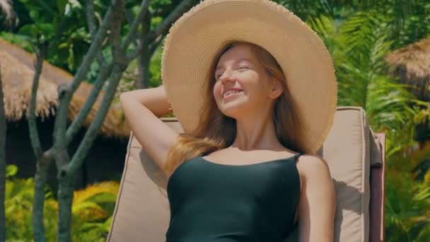 魅力的な幸せな女性は海での夏のビーチ休暇に屋外の自然をお楽しみください 現代の熱帯リゾートの近くのビーチチェアで休暇中にリラックスした笑顔の女性旅行者 背景にヤシの木 — ストック動画