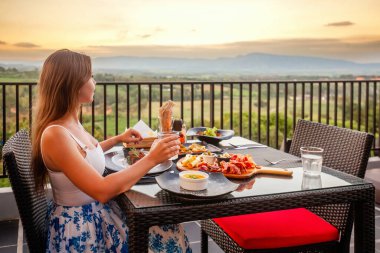 Dinner with sunset mountain view. Elegant woman in luxury outdoor restaurant. Leisure, holidays, travel concept.